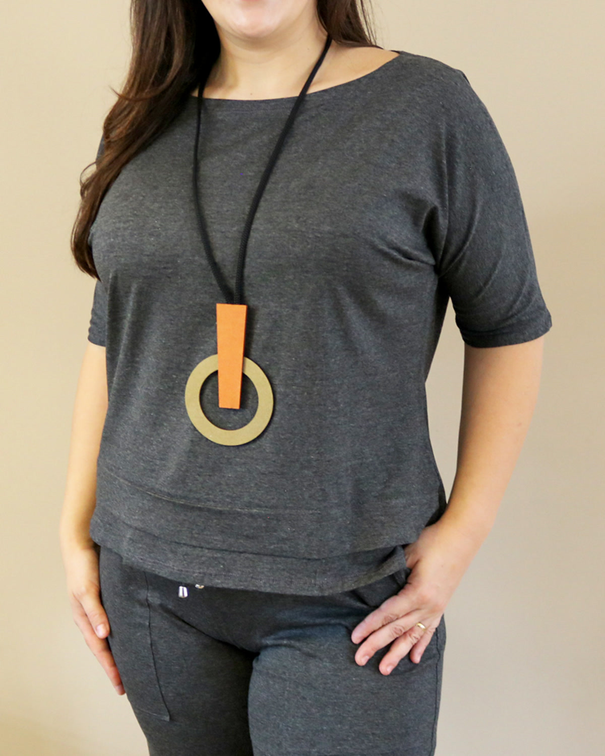 Mulher com blusa cinza usando o Colar Formas Laranja, com forma circular clara e peça vertical laranja